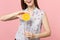 Cropped image of young woman in summer clothes holding half of fresh ripe orange fruit, glass cup isolated on pink