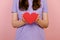 Cropped images of young female blogger holds in hands little red heart, isolated over pink studio background. Like blogging blog