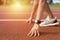 Cropped low angle of female athlete on the starting point of a running track with daylight, preparing for a