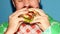 Cropped male face. Man biting delicious burger with meat, bacon, cheese, salad and vegetables against colorful