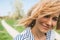 Cropped outdoor closeup portrait of attractive female with blonde blowing hair, smiling and looking at the camera. Closeup view of