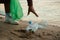 Cropped photo of African woman picking up spilled trash from sand on beach in green plastic bag. Ecology, pollution.