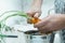 Cropped photo of man wearing grey apron cutting off leaves at top of carrot with knife over metal bowl full of peelings.