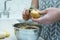 Cropped photo of man wearing grey apron peeling potato with green peeler over metal bowl. Organic waste management.