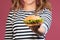 Cropped photo of smiling girl in striped t-shirt showing hamburger