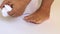 Cropped photo of woman standing on white background, taking off white cotton socks and folding on floor. Close-up.