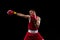 Cropped portrait of one professional boxer in red uniform training isolated over black background. Straight punch