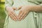 Cropped pregnant woman holds hands in heart shape