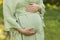 Cropped pregnant woman puts,holds hands on big