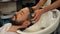 Cropped shot of barber washing head to handsome bearded man at barbershop