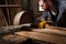 cropped shot of bearded carpenter in protective gloves and googles using machine saw