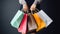 Cropped shot of female hand holding bunch of different colorful blank shopping bags over isolated black background. AI Generative