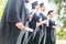 cropped shot of graduated students in capes and hats holding