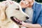 cropped shot of people stroking golden retriever dog with tongue out in park