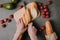 cropped shot of person cutting baguette on wooden board, avocados and fresh tomatoes on grey