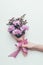 Cropped shot of person holding beautiful elegant bouquet of tender purple flowers with ribbon