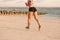 cropped shot of sportswoman with smartphone in running armband case jogging on beach