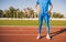 Cropped shot of a sprinter athlete male standing on a running track with hands on waist. Runner man standing at the line race