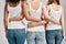 Cropped shot of three diverse friendly women in white shirt and casual denim jeans putting arms around each other while