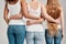 Cropped shot of three diverse friendly women in white shirt and casual denim jeans putting arms around each other while