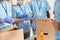 Cropped shot of volunteers in blue uniform, protective masks and gloves sorting, packing canned food in cardboard box