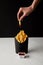 cropped shot of woman folding french fry poured into ketchup over box of fries isolated on black