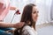 cropped shot of woman hairdressing female friend by hair straightener on sofa