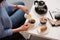 cropped shot of woman pouring cream into cup of coffee with cane sugar and piece of cake