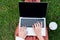 cropped shot of woman working with laptop while sitting on grass with paper cup
