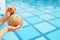 Cropped shot of young woman holding in hands whole coconut cocktail with straw in the hole over outdoor swimming pool with square