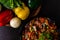 Cropped top view shot of delicious Chilli Chicken along side colorful vegetables on wooden surface