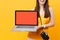Cropped tourist woman holding laptop pc computer with blank black empty screen isolated on yellow orange background