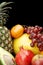 Cropped vertical view of many colorful fruits on black with reflection