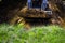 Cropped view of bulldozer loaded with soil in dirty pit with grass on foreground