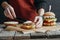 cropped view of girl in apron making tasty homemade cheeseburgers on baking paper