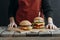 cropped view of girl in apron standing at wooden table with tasty cheeseburgers