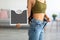 Cropped view of Indian woman in oversized jeans holding scales, impressed with results of weight loss diet