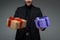 Cropped view of male in black suit holding two gift boxes isolated on grey, international womens day concept