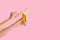 Cropped view of millennial girl peeling ripe banana on pink background, close up. Copy space