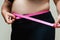 Cropped view of overweight woman measuring waist with tape measure at home, close up. Unrecognizable European woman
