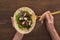 Cropped view of woman eating falafel with vegetables and sauce on pita with fork on wooden table.