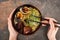 Cropped view of woman eating spicy meat ramen with chopsticks on stone surface