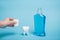 Cropped view of woman holding cap near tooth model and bottle of mouthwash on blue background.