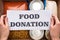 Cropped view of woman holding card with food donation lettering above box with cans and groats