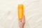 Cropped view of woman holding orange sunscreen lotion above golden sand.