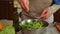 Cropped view of a woman seasoning a healthy vegan salad, putting sesame seed and pouring olive oil over raw vegetables