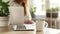 Cropped view of woman sitting at wooden table and working on laptop. A cup of coffee with a potted plant in the