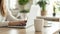 Cropped view of woman sitting at wooden table and working on laptop. A cup of coffee with a potted plant in the