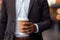 Cropper view of A businessperson holding a coffee cup stands isolated against a softly blurred background. AI Generated