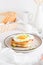 Croque madam sandwich with cheese, ham and egg on a plate on a light table. Hearty homemade breakfast. Vertical view